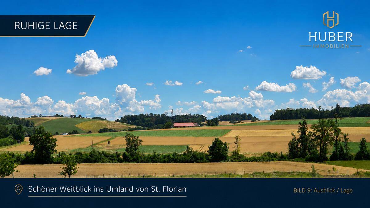 Weitläufige Landschaft mit Feldern und Bäumen unter blauem Himmel, die eine ruhige Umgebung zeigt.
