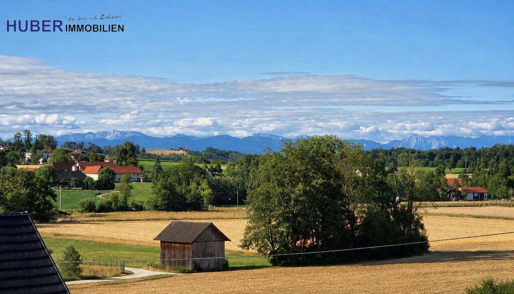 Panoramablick über eine ländliche Gegend mit Feldern, Häusern und majestätischen Bergen am Horizont.