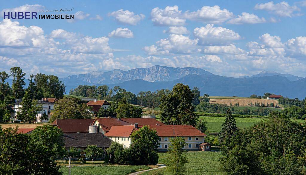 Idyllischer Blick auf eine ländliche Siedlung mit grünen Bäumen und beeindruckendem Bergpanorama.