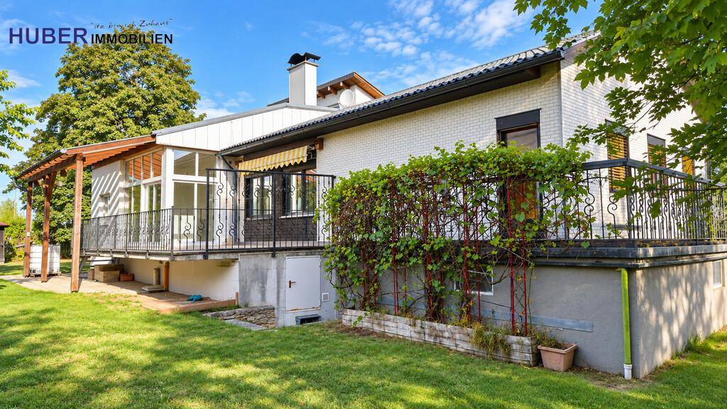 Rückseite des Hauses mit großem Balkon, Rankpflanzen und einem weitläufigen Gartenbereich.