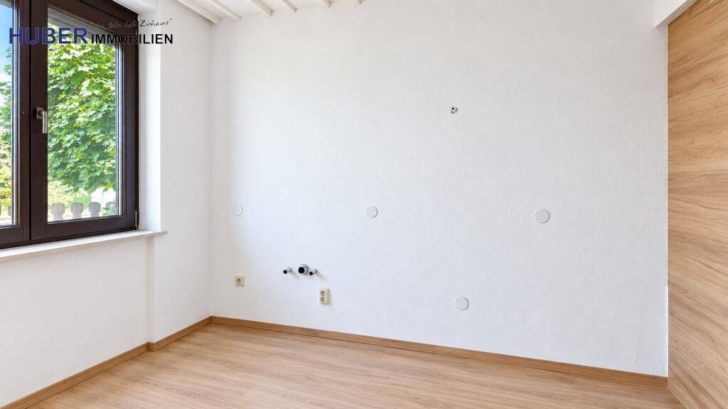 Ecke eines Raumes mit Fenster und sichtbaren Wasseranschlüssen für zukünftige Installationen.