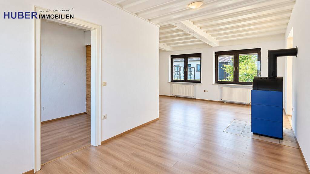 Geräumiges Wohnzimmer mit Kaminofen, Holzbalkendecke und hellem Laminatboden.