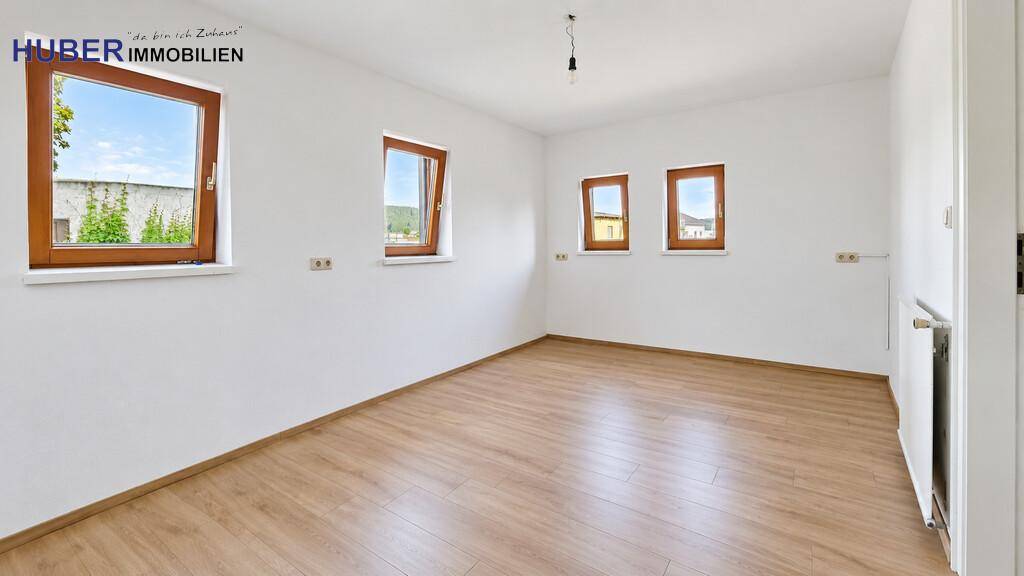 Leeres Schlafzimmer mit Laminatboden und mehreren Fenstern für viel Tageslicht.