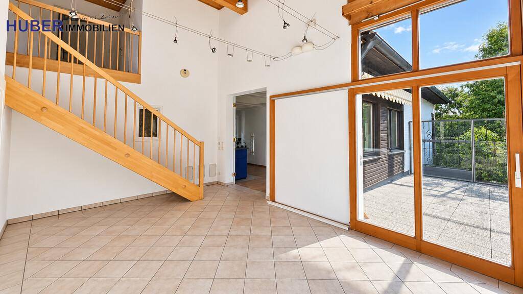 Offener Wohnbereich mit Fliesenboden, Holztreppe und großzügigem Wintergarten-Zugang.