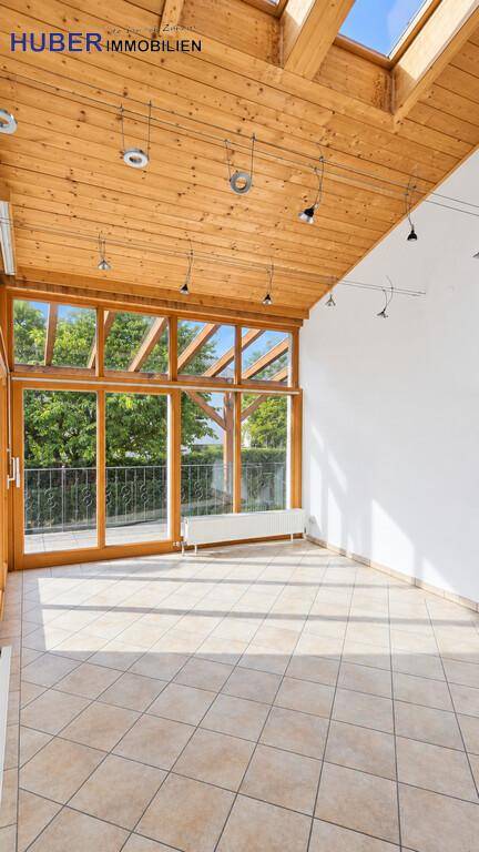 Heller Wintergarten mit Holzdachkonstruktion, Fliesenboden und Blick ins Grüne.
