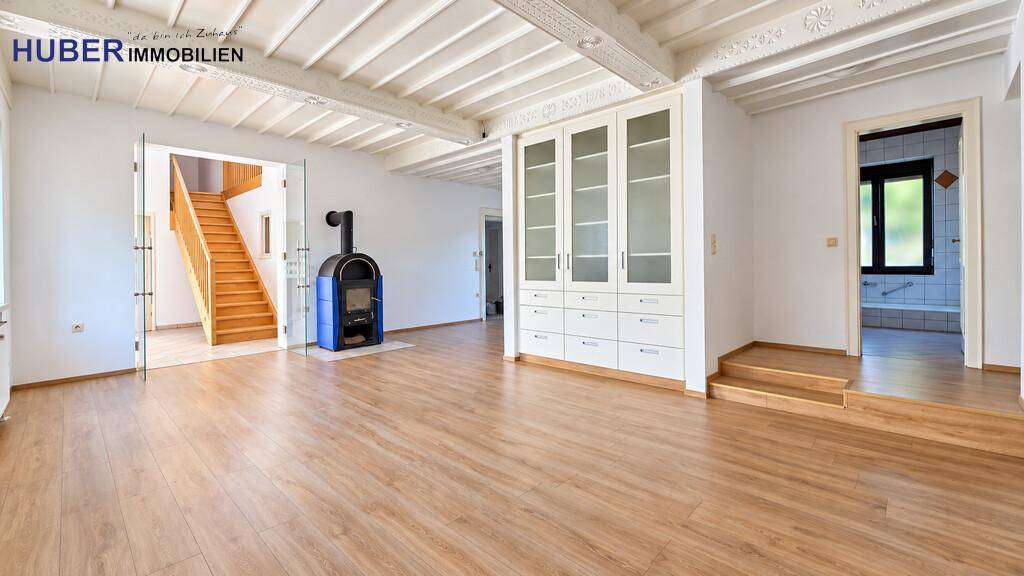 Offener Wohnbereich mit Kaminofen, Holztreppe und Zugang zum Badezimmer.