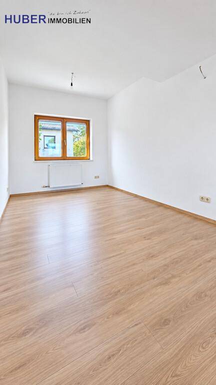 Helles, leeres Zimmer mit Laminatboden und einem Fenster, das viel Licht hereinlässt.