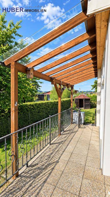 Überdachte Terrasse mit Holzpergola, Glasdach und Blick in den Garten.