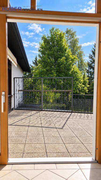 Blick von innen auf eine sonnige Terrasse mit Steinplatten und schmiedeeisernem Zaun.