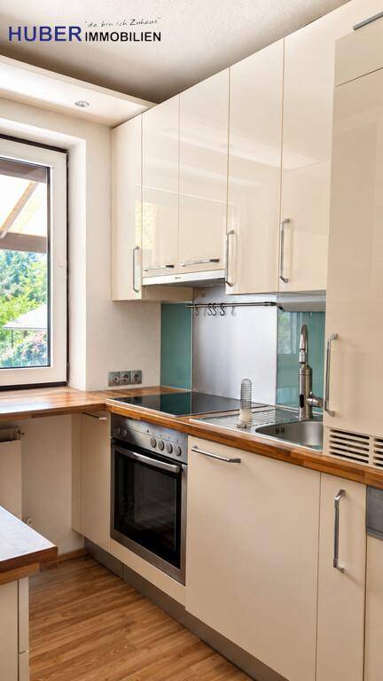 Moderne Einbauküche mit hellen Fronten, Holzarbeitsplatte und Fenster für Tageslicht.
