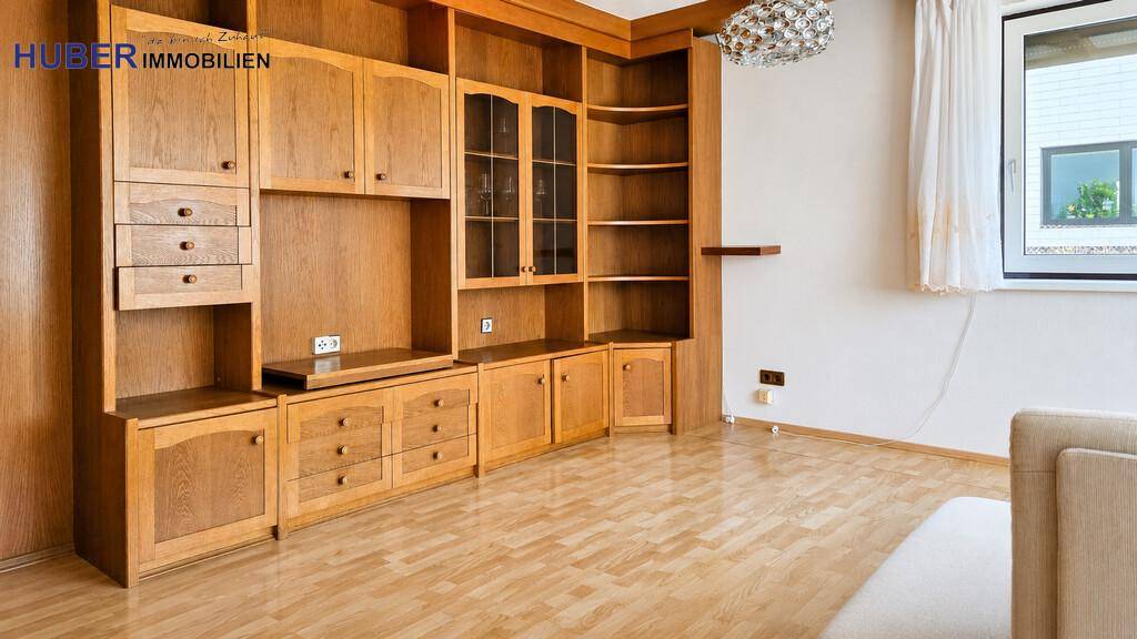 Wohnzimmer mit großer Holzschrankwand, Laminatboden und Blick auf den Außenbereich.