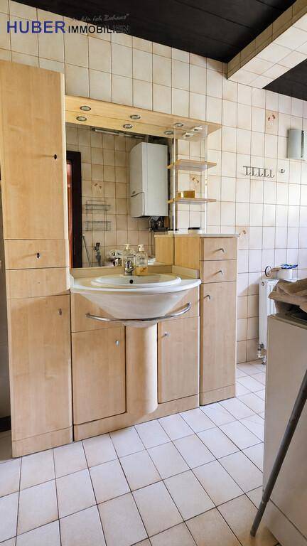 Badezimmer mit hellem Holzwaschtisch, Spiegelschrank und beigefarbenen Fliesen.