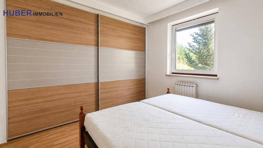 Schlafzimmer mit großem Einbauschrank, Laminatboden und Fenster mit Blick ins Grüne.