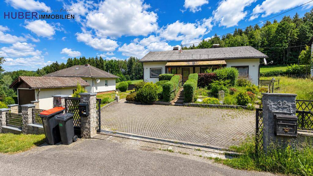 Einfamilienhaus mit gepflasterter Auffahrt und umzäuntem Vorgarten in ländlicher Umgebung.