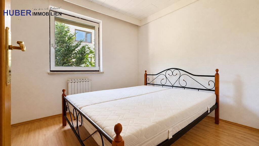Helles Schlafzimmer mit Doppelbett, Laminatboden und Fenster mit Blick ins Grüne.