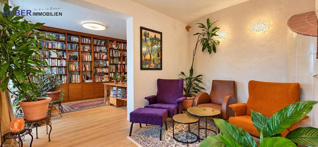 Gemütlicher Wohnbereich mit großer Bücherwand, bequemen Sesseln und vielen Grünpflanzen.