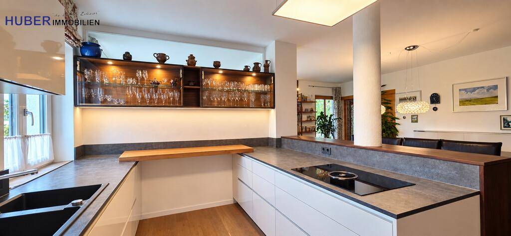 Moderne Küche mit Induktionskochfeld, Spüle und eleganten Glasvitrinen für Geschirr.