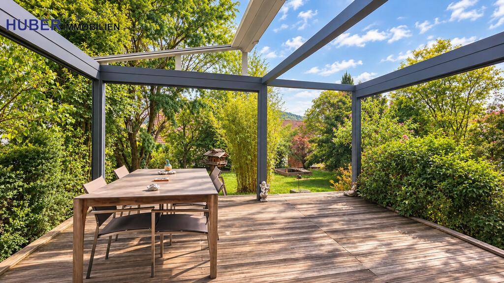 Große Holzterrasse mit Esstisch und Überdachung, umgeben von üppigem Grün.