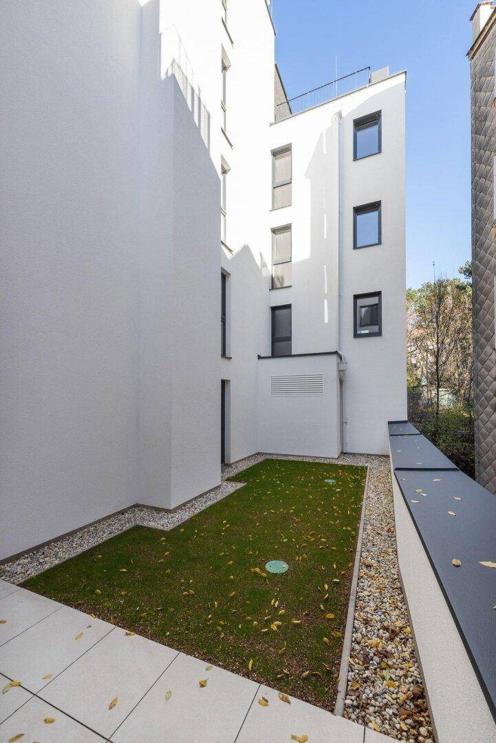 Ruhiger Gartenbereich mit Rasen und Kieswegen, umgeben von der modernen Architektur des Gebäudes.