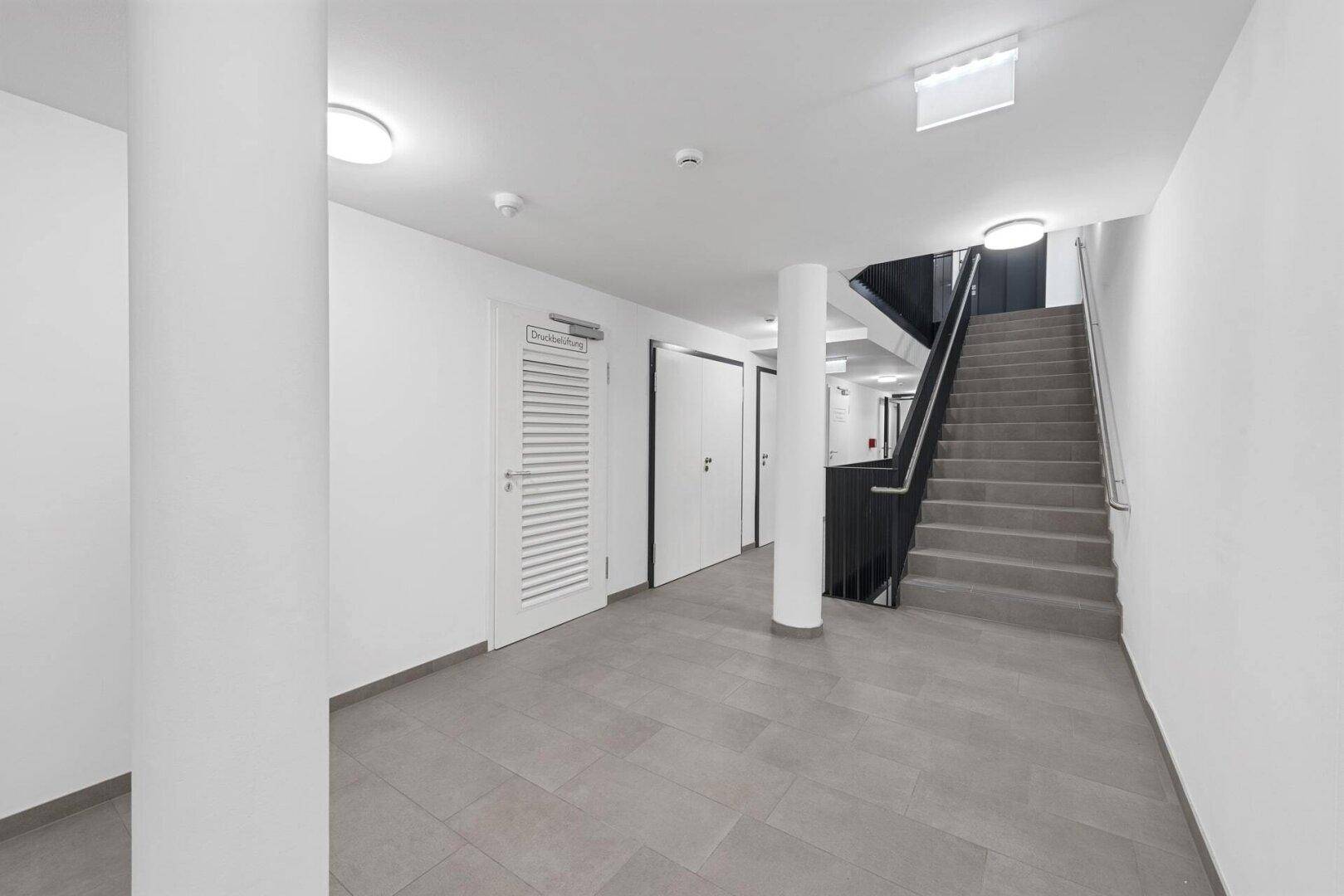 Heller Eingangsbereich mit Treppenhaus und Fliesenboden in einem modernen Gebäude.