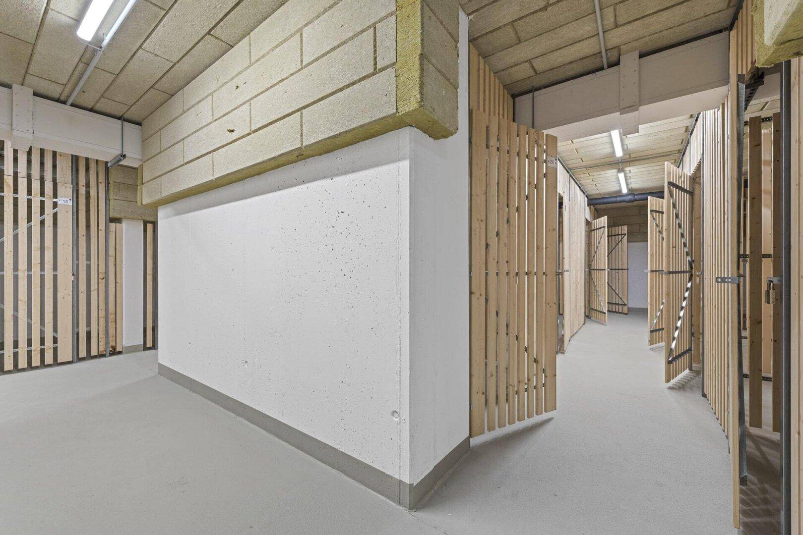 Kellerabteile mit Holzlattenwänden und Betonboden, bieten zusätzlichen Stauraum.