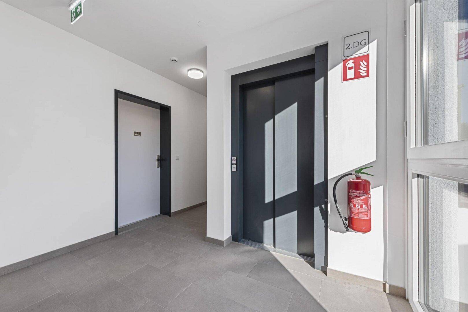 Moderner Flur mit Aufzug und Fliesenboden im Eingangsbereich eines Wohnhauses.