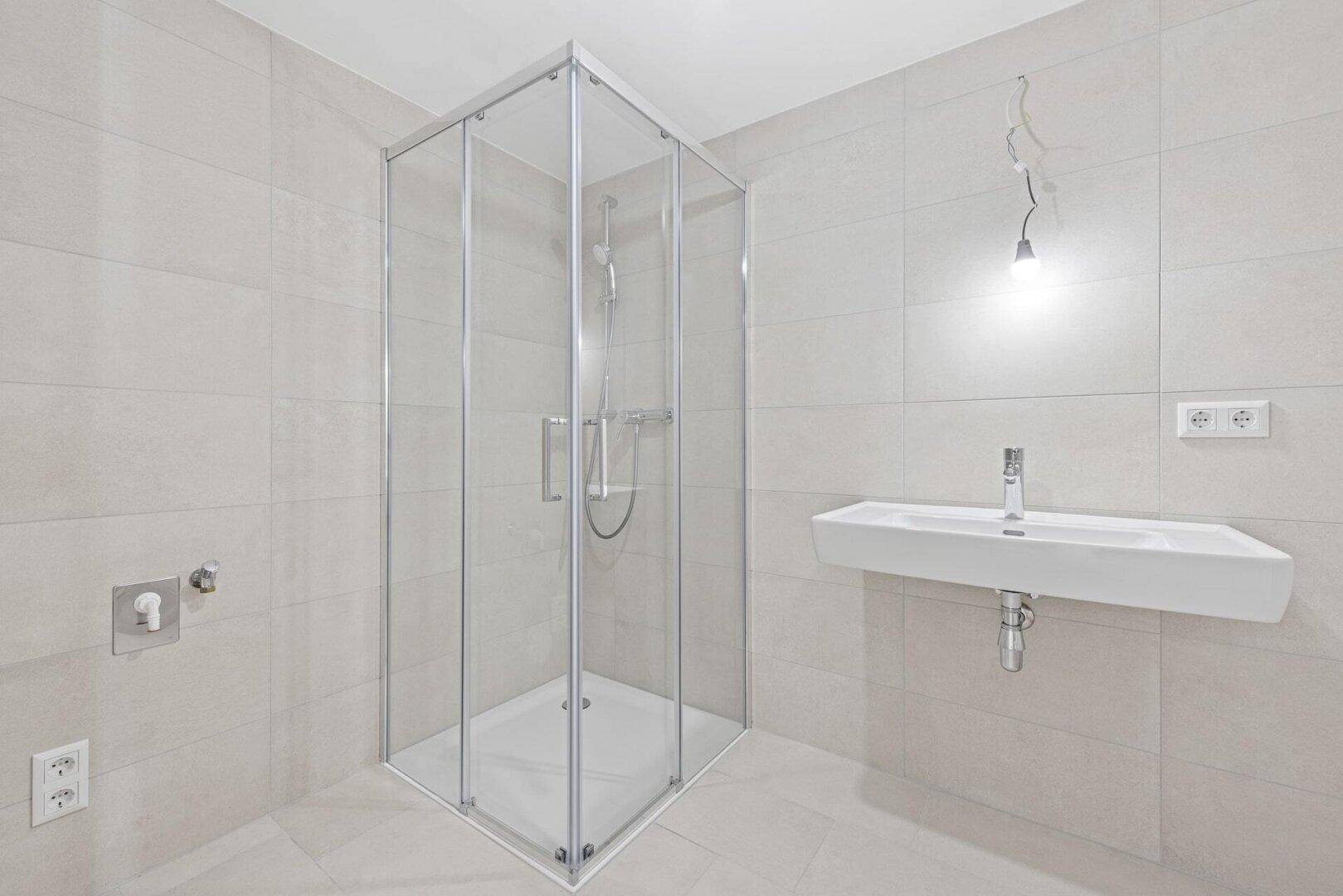 Modernes Badezimmer mit Duschkabine, wandhängendem Waschbecken und hellen Fliesen.