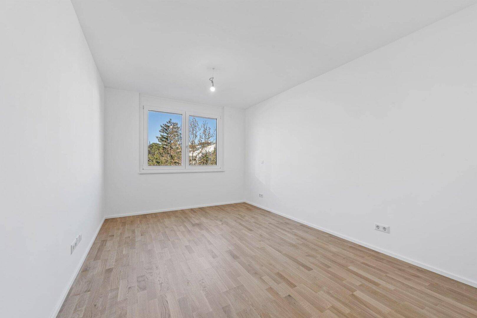 Helles Schlafzimmer mit Parkettboden und großem Fenster, bereit zur individuellen Gestaltung.