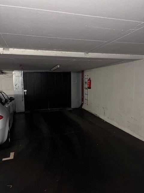 Tiefgaragenstellplatz mit Feuerlöscher an der Wand und einem großen schwarzen Garagentor im Hintergrund.
