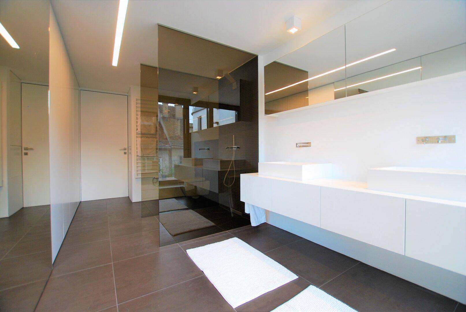 Modernes Badezimmer mit Doppelwaschbecken, begehbarer Dusche und großen Spiegeln, hell und funktional.