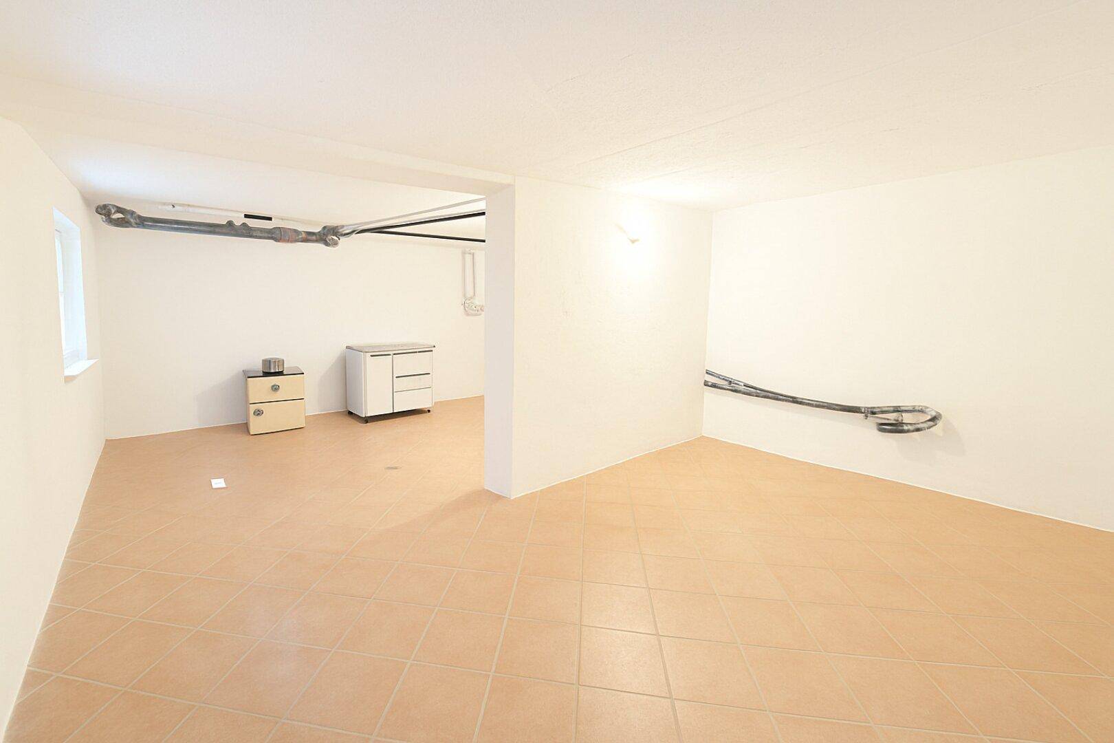 Heller Raum mit Fliesenboden, sichtbaren Leitungen und einem kleinen Fenster, ideal als Hauswirtschaftsraum.