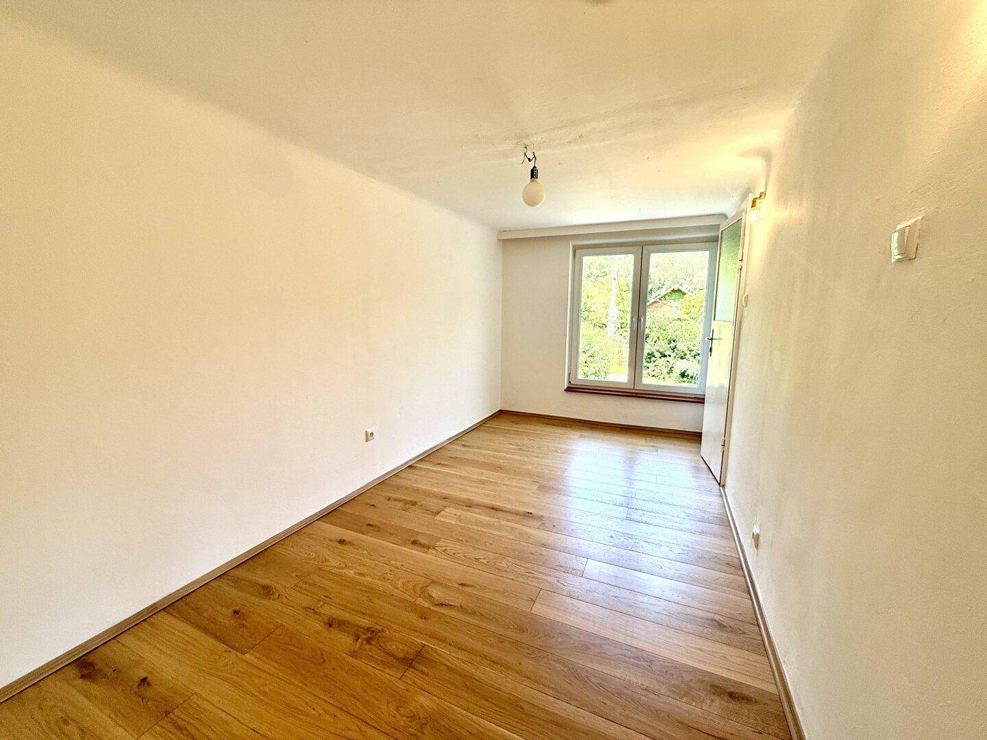 Geräumiges Zimmer mit glänzendem Holzfußboden und einem Fenster, das viel Tageslicht hereinlässt.