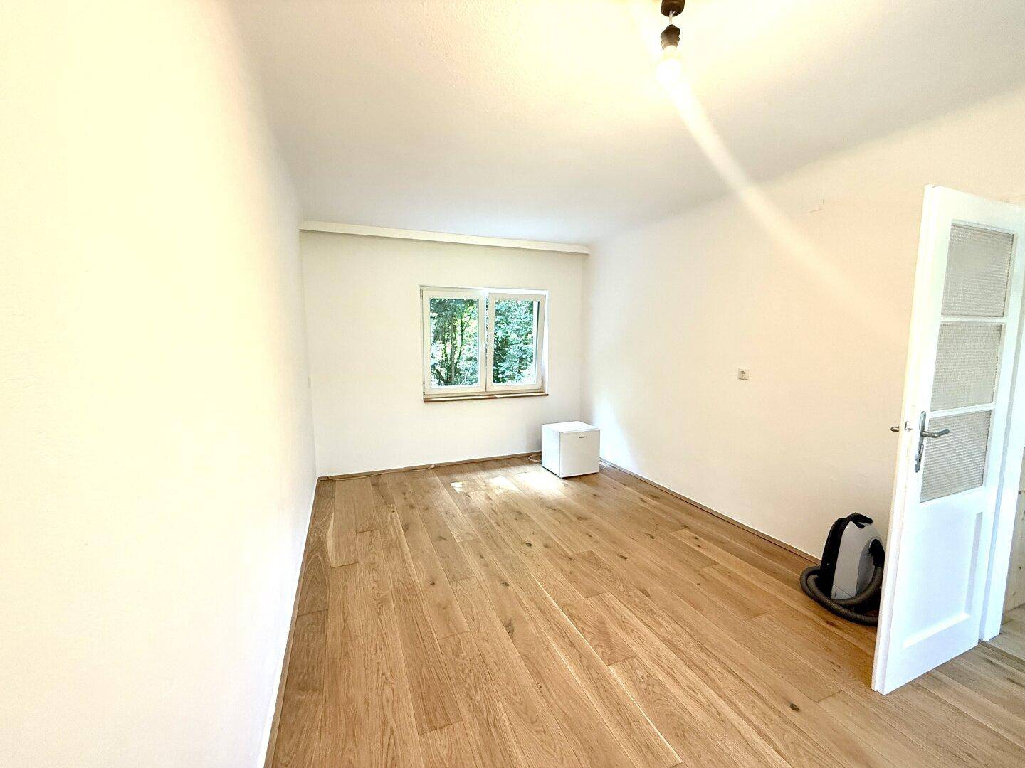 Helles Zimmer mit Holzboden und Fenster, das einen ruhigen Blick auf die umliegende Natur bietet.