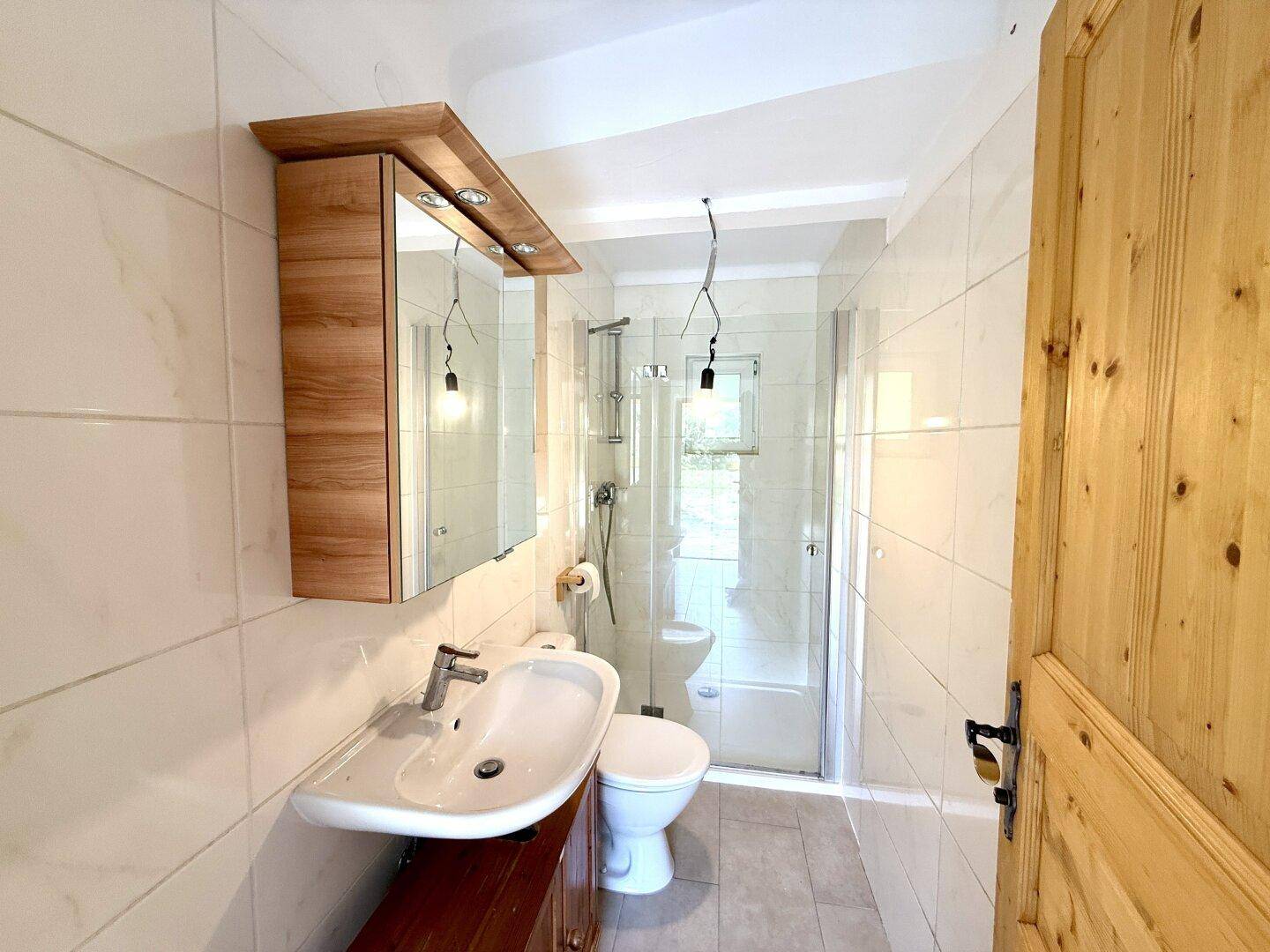 Modernes Badezimmer mit hellen Fliesen, Waschtisch, Spiegelschrank und einer Duschkabine.