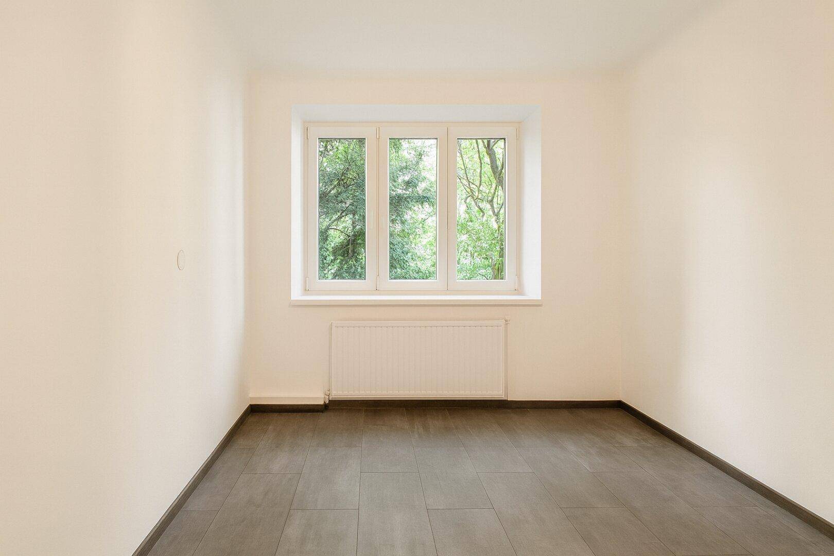 Heller, leerer Raum mit großem Fenster und Blick ins Grüne.