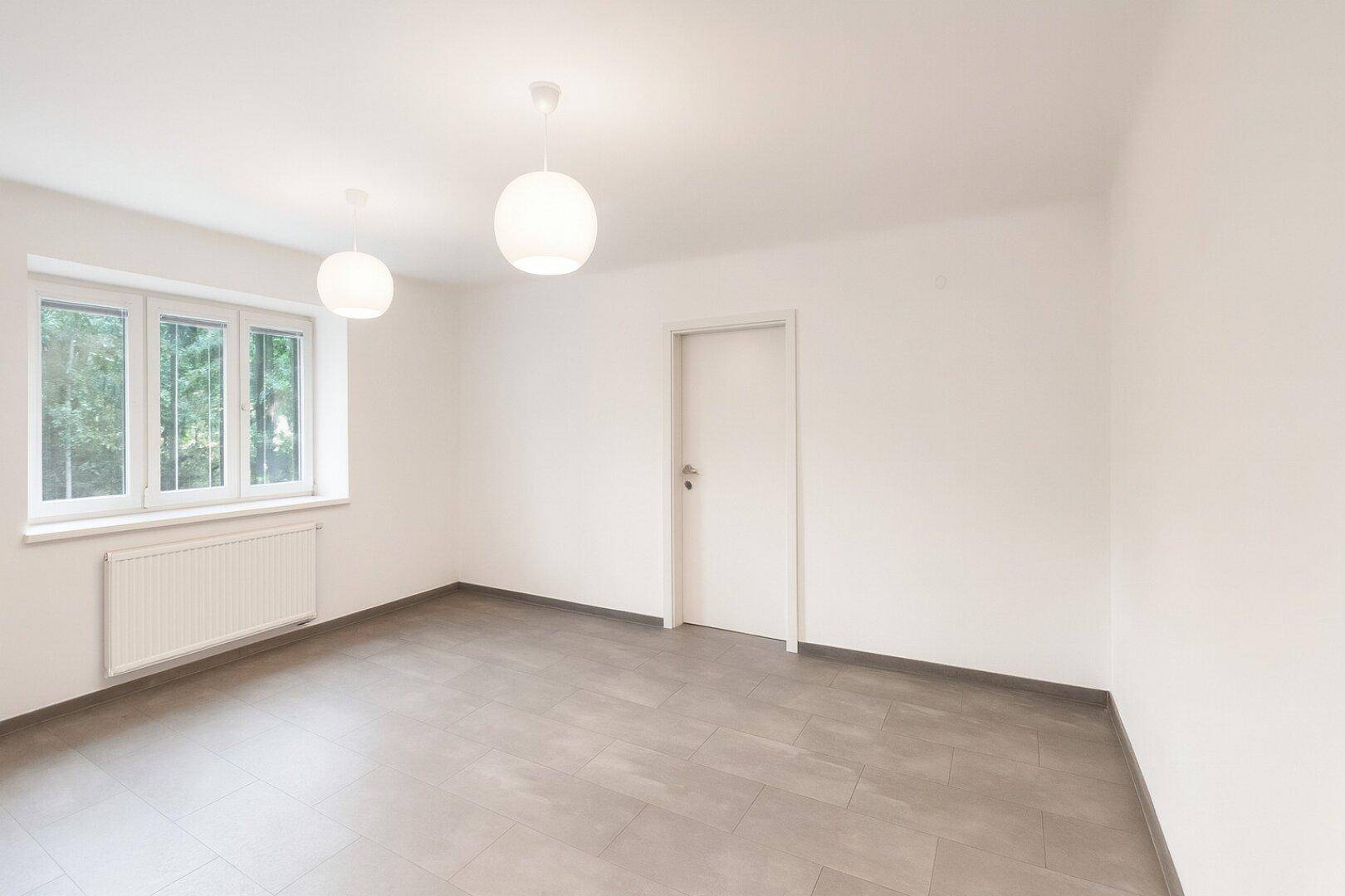 Leerer Raum mit großen Fenstern und Fliesenboden, bereit zur individuellen Gestaltung.