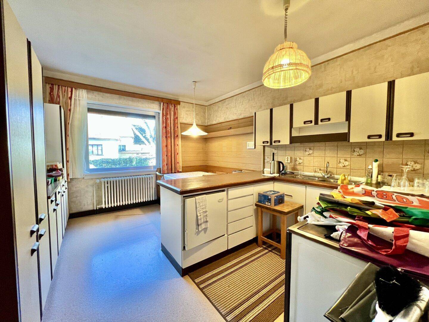 Funktionale Küche mit weißen Schränken, Fliesenrückwand und einem Fenster mit Blick nach draußen für Tageslicht.