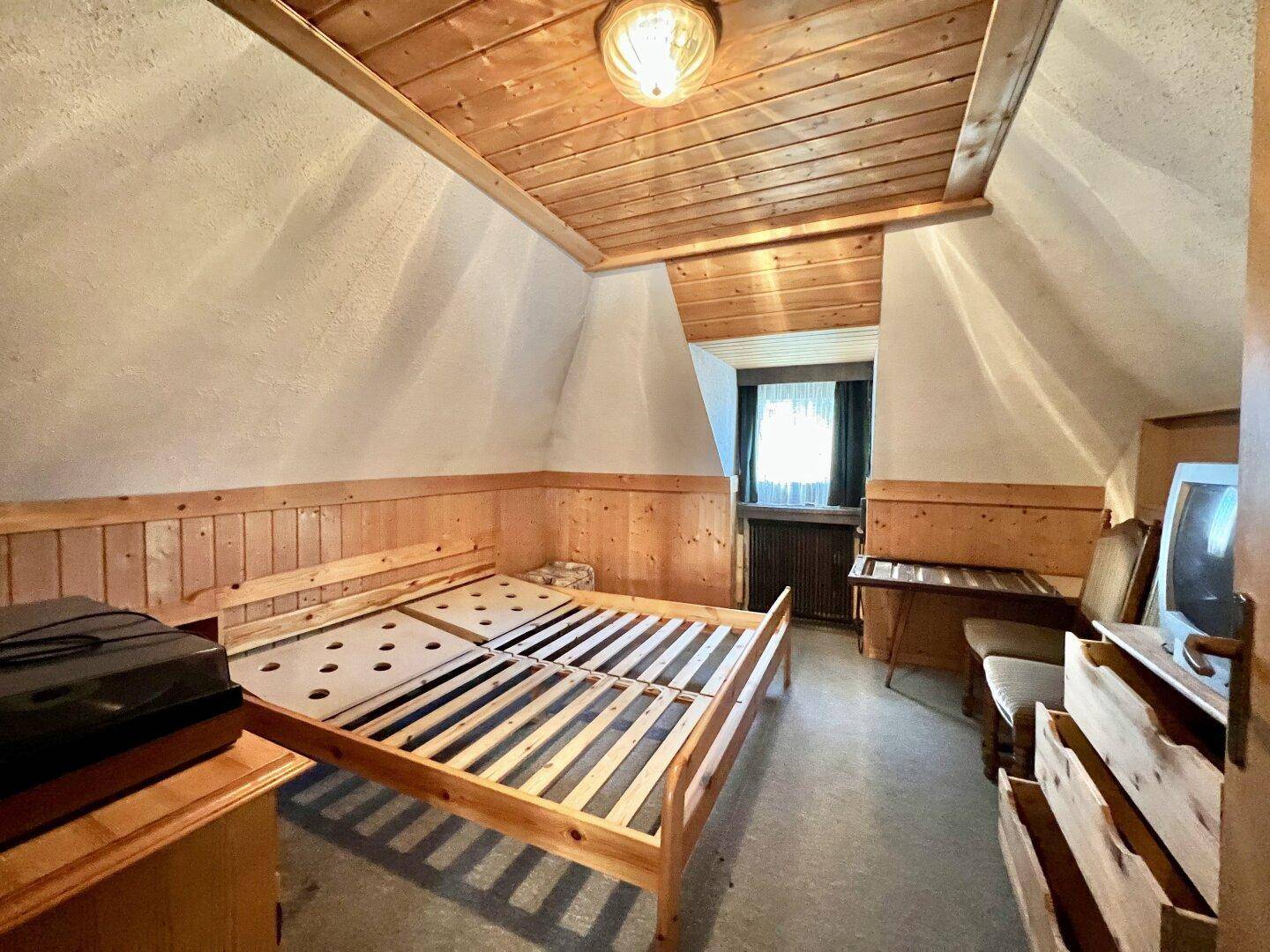 Gemütliches Schlafzimmer im Dachgeschoss mit Holzdecke und Holztäfelung an den Wänden für eine warme Atmosphäre.