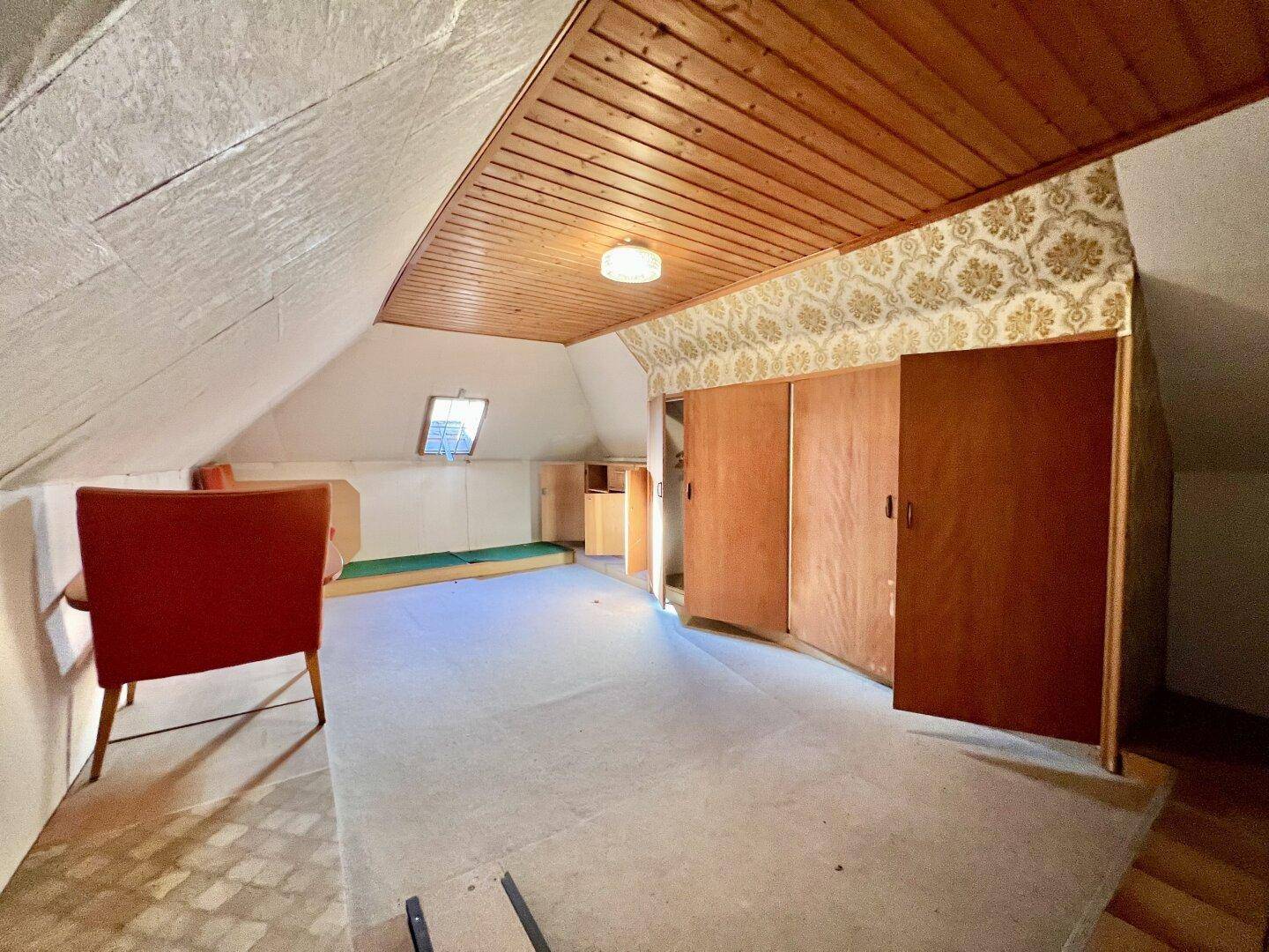 Dachgeschossraum mit schräger Decke, Holzschränken und einem Dachfenster für Tageslicht und Belüftung.