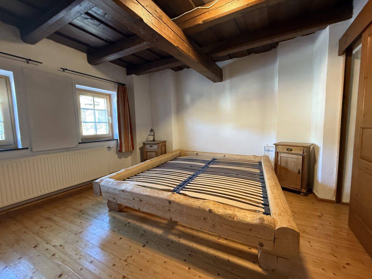Schlafzimmer mit rustikalem Holzbett, Holzdielenboden und sichtbaren Deckenbalken.