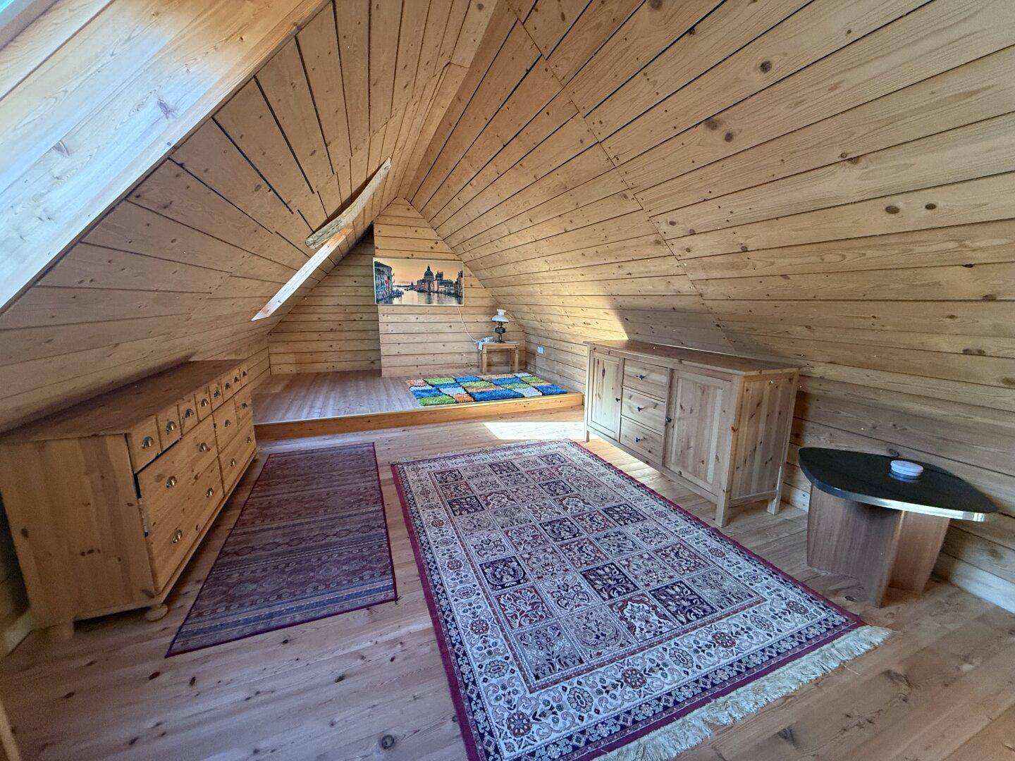 Gemütlicher Dachbodenraum mit Holzverkleidung, Holzdielenboden und schrägen Wänden.