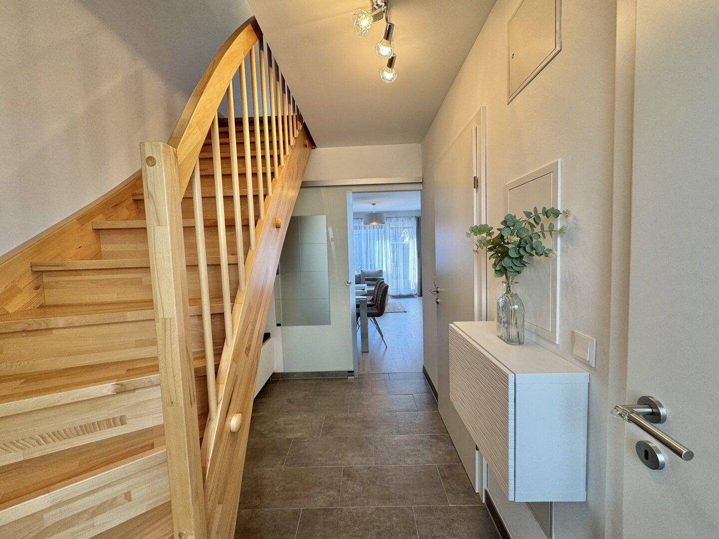 Heller Eingangsbereich mit eleganter Holztreppe und Fliesenboden, der zu den oberen Etagen führt.