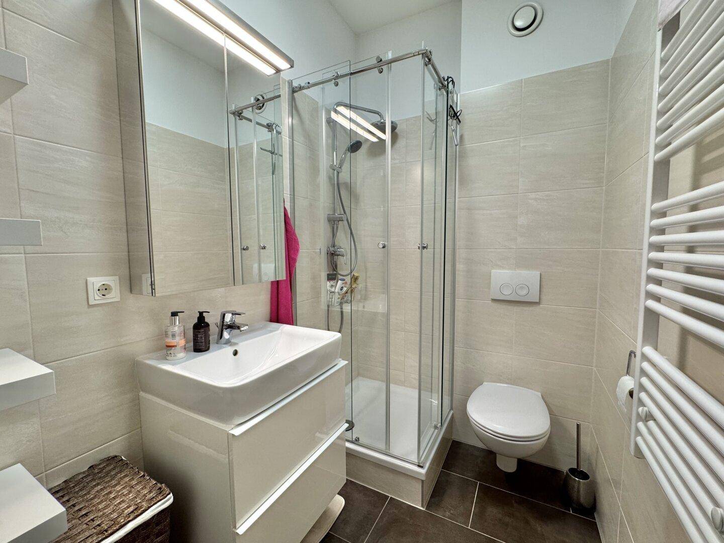 Modernes Badezimmer mit Duschkabine, wandhängendem WC und beheiztem Handtuchhalter.