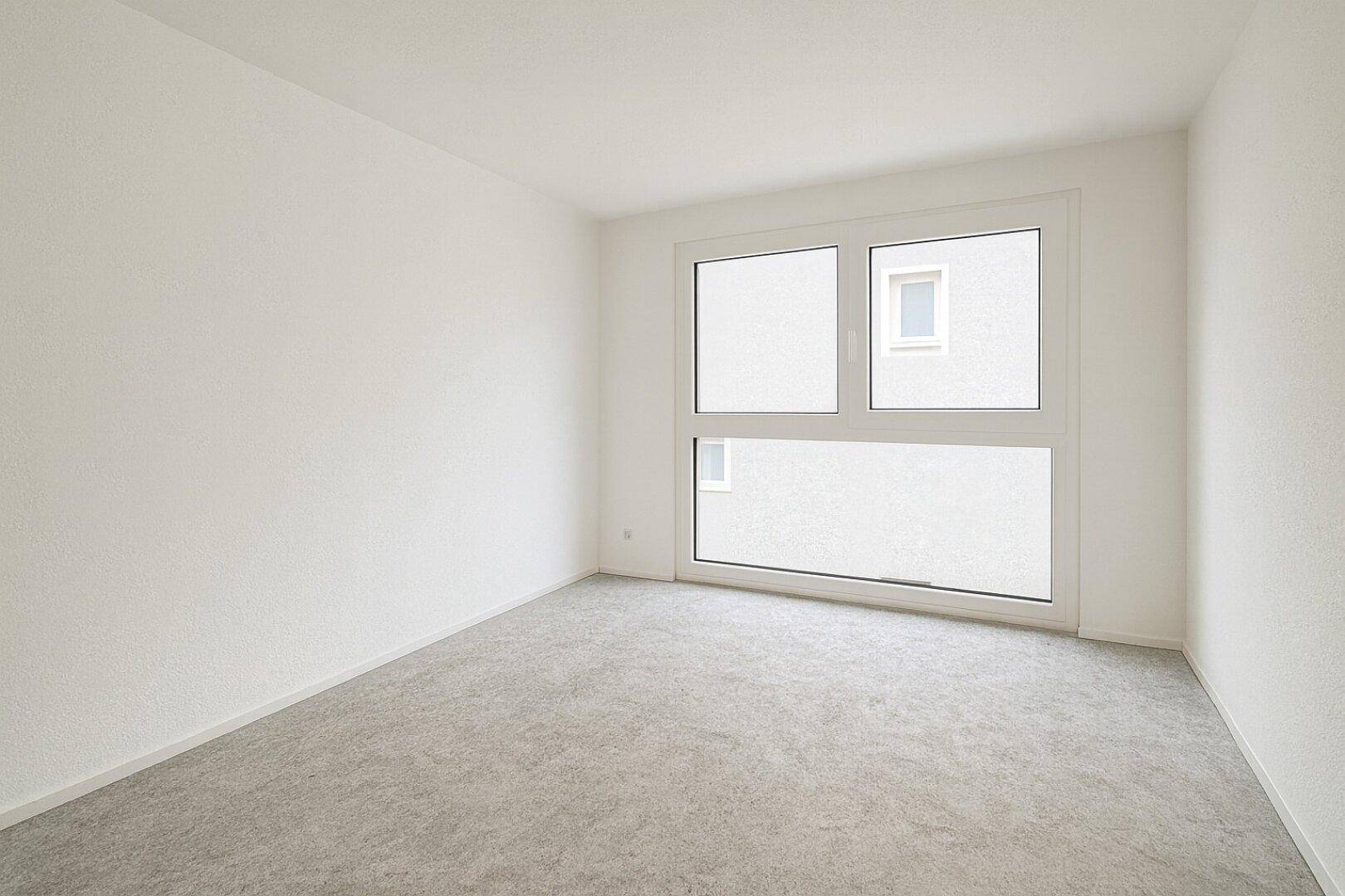 Leeres Zimmer mit hellem Boden und großem Fenster, ideal als Kinder- oder Gästezimmer.
