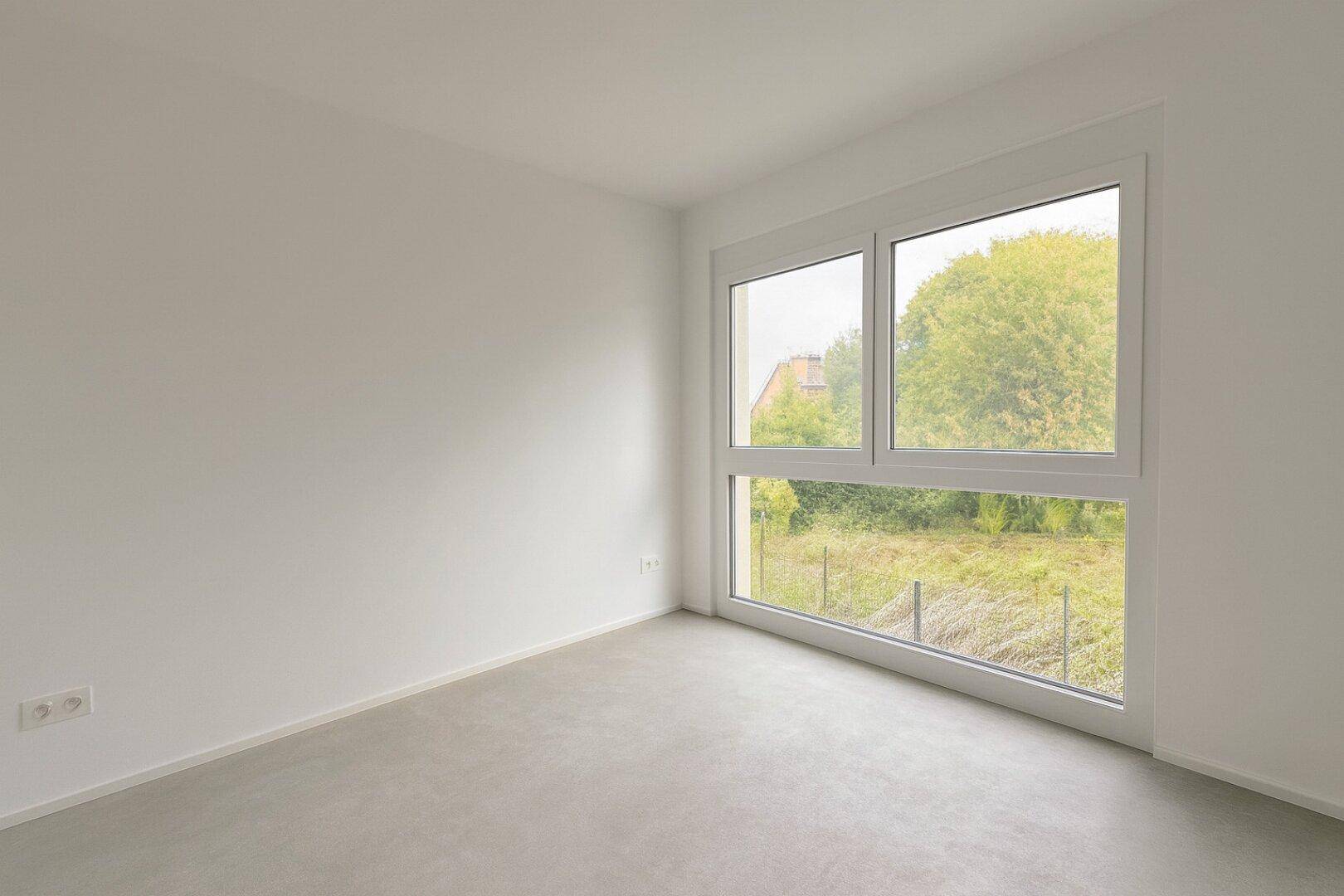 Leeres Zimmer mit großem Fenster und Rohbetonboden, bereit für neue Einrichtung.