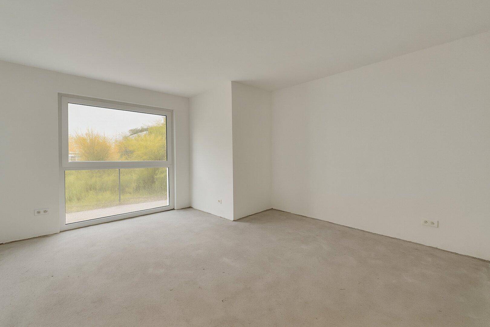 Leeres Zimmer mit großem Fenster und Rohbetonboden, ideal für ein Schlafzimmer.