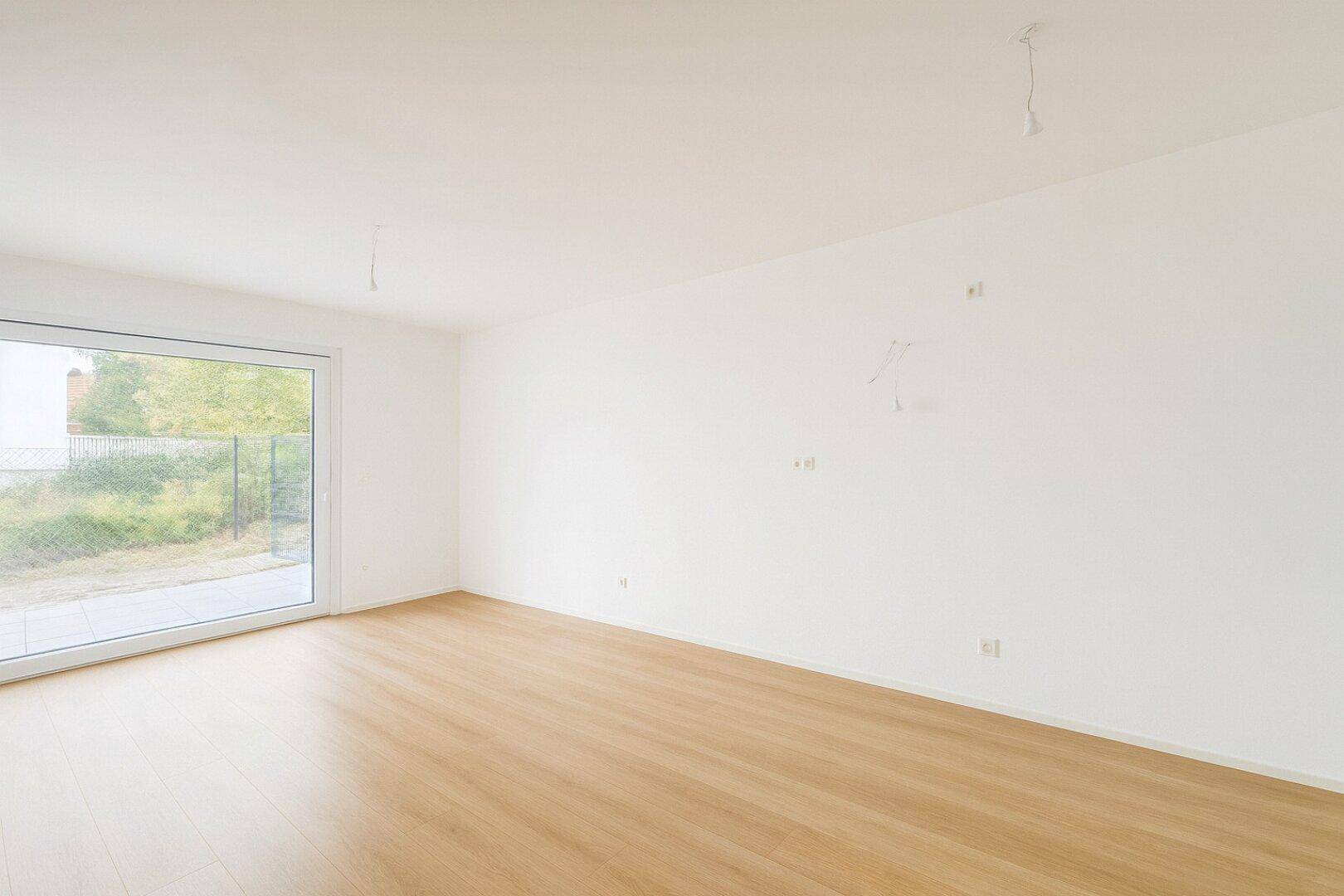 Heller, leerer Wohnraum mit großem Fenster und Parkettboden, bereit zur individuellen Gestaltung.