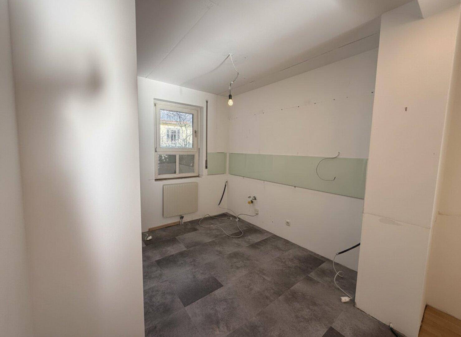 Leerer Raum mit Fliesenboden und vorbereiteten Anschlüssen, möglicherweise eine zukünftige Küche.