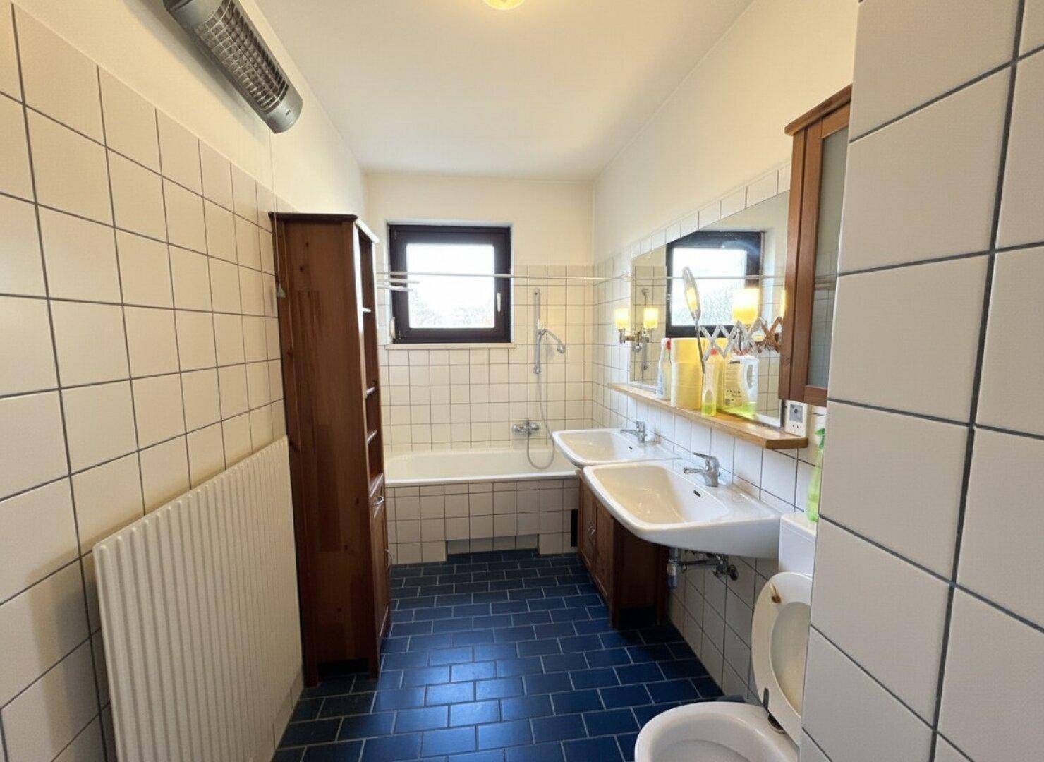 Badezimmer mit zwei Waschbecken, Badewanne und blauen Bodenfliesen.