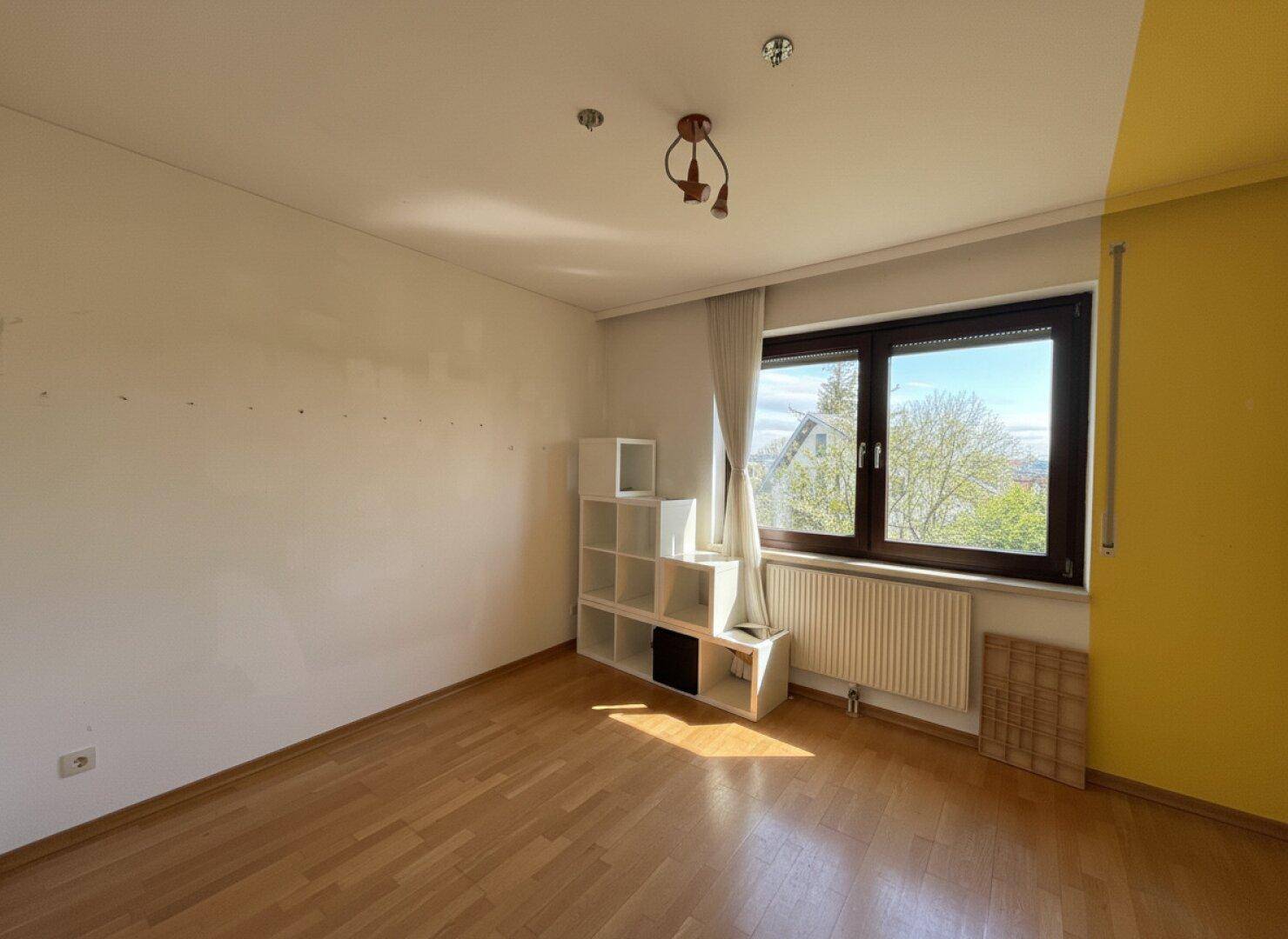 Leerer Raum mit gelber Akzentwand, Holzboden und großem Fenster.